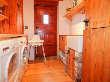 A laundry room with washing machines a wooden door a high chair and a sink at The Wagon House Tresmeer near Launceston