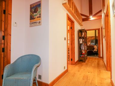 A hallway with wooden floors a blue wicker chair a bookshelf and exposed wooden beams at The Wagon House in Tresmeer near Launceston