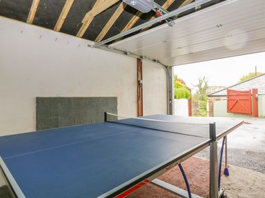 A garage with a ping pong table and an open garage door showing an outdoor area at The Wagon House in Tresmeer near Launceston