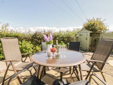 An outdoor patio with a round glass table surrounded by chairs and a garden shed in the background at The Wagon House in Tresmeer near Launceston