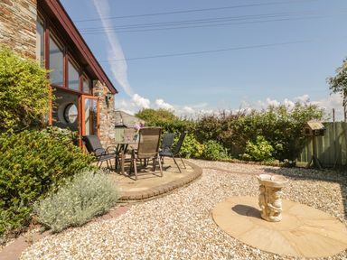 An outdoor patio area with chairs and a table next to a stone building with a circular birdbath in a gravel yard at The Wagon House in Tresmeer near Launceston