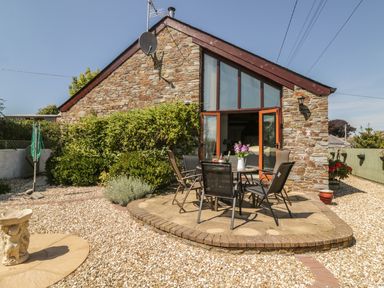 An outdoor patio area with a round table and four chairs outside a stone house with large windows at The Wagon House in Tresmeer near Launceston