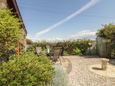 A garden patio with four chairs around a table next to a stone house and a birdbath at The Wagon House in Tresmeer near Launceston
