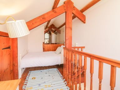 A loft bedroom with a single bed white bedding wooden beams wooden railing and a striped rug at The Wagon House in Tresmeer near Launceston