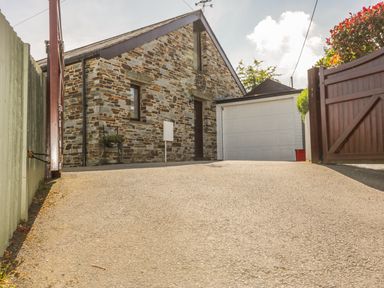 A stone house with a driveway leading to a white garage door and a wooden gate at The Wagon House in Tresmeer near Launceston