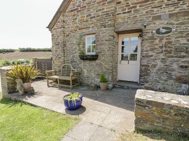 A stone cottage entrance with a wooden bench and potted plants at Dovecote in Gorran Haven