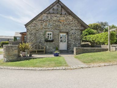 A stone cottage with a white door and window a wooden bench and potted plants outside at Dovecote in Gorran Haven