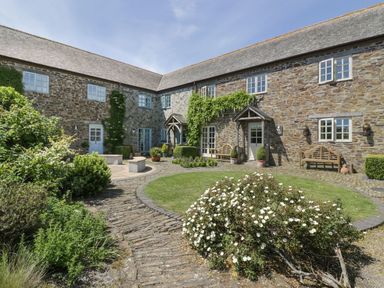 A courtyard with stone buildings surrounded by benches plants and flowers at Dovecote in Gorran Haven