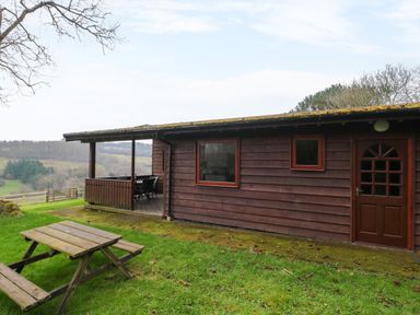 A wooden cabin with a picnic table on grass and a covered porch with chairs and a table at The Ash Lodge near Lyme Regis