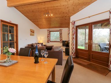 A living room and dining area with a wooden ceiling and double doors leading outside at The Ash Lodge near Lyme Regis