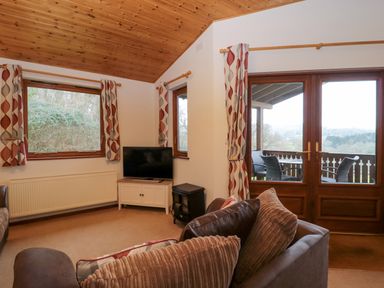 A living room with sofas a television and large windows overlooking a balcony at The Ash Lodge near Lyme Regis