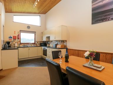 A kitchen with white cabinets a dining table with black chairs and a bottle with glasses at The Ash Lodge near Lyme Regis