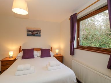 A bedroom with a double bed two purple pillows two bedside tables with lamps and a window with curtains at The Ash Lodge near Lyme Regis