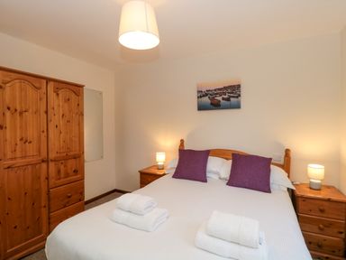 A bedroom with a double bed two purple pillows two bedside tables with lamps a wooden wardrobe and a picture on the wall at The Ash Lodge near Lyme Regis