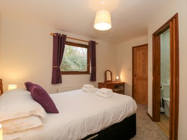 A bedroom with a bed towels on it a window with curtains a desk with a mirror and a door leading to a bathroom at The Ash Lodge near Lyme Regis