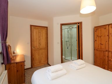 A bedroom with a bed and towels a wooden wardrobe a dresser a door and an ensuite bathroom at The Ash Lodge near Lyme Regis