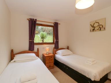 A bedroom with two single beds with white linens a wooden nightstand with a lamp and a window with purple curtains at The Ash Lodge near Lyme Regis