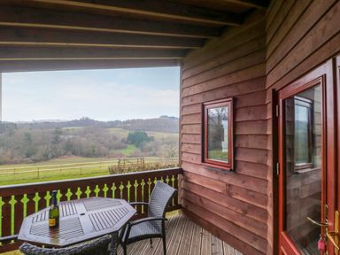 A wooden balcony with a table and chairs overlooking fields and hills at The Ash Lodge near Lyme Regis