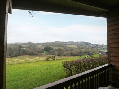 A view of green fields with a wooden fence a swing set and hills in the background from a wooden porch at The Ash Lodge near Lyme Regis
