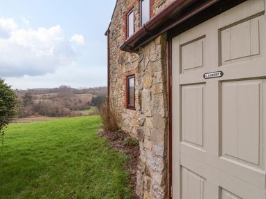 A stone house exterior with a door labeled laundry and a grassy field with trees in the background at The Ash Lodge near Lyme Regis