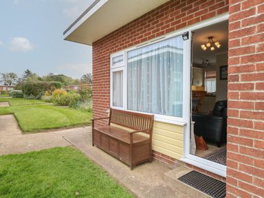 A wooden bench outside a brick house with a glass door open to a living area at En-Casa in Mundesley
