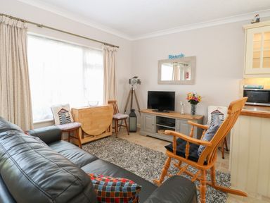 A living room with a black leather sofa wooden rocking chair TV on a stand and a small dining table at En-Casa in Mundesley
