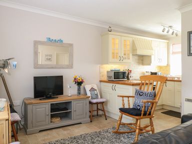 A living room with a wooden rocking chair and a television on a cabinet next to a kitchen at En-Casa in Mundesley