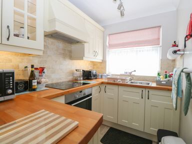 A kitchen with wooden countertops white cabinets a window with a striped blind and various appliances at En-Casa Mundesley