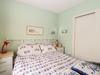 A bedroom with a bed with patterned bedding two nightstands with red lamps and a closet with sliding doors at En-Casa in Mundesley
