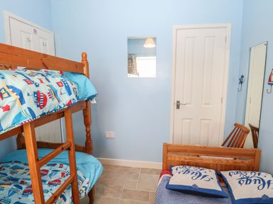 A small bedroom with wooden bunk beds and a single bed with pillows a wooden chair and two doors at En-Casa Mundesley