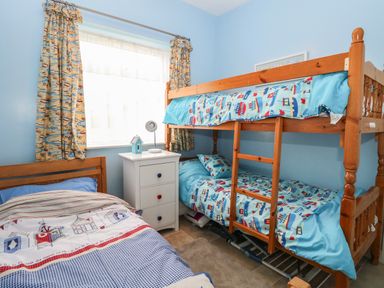 A bedroom with a bunk bed a single bed a white chest of drawers and a window with patterned curtains at En-Casa in Mundesley