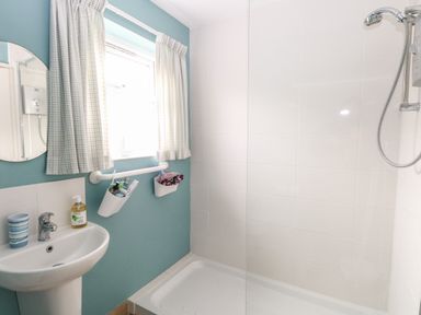 A bathroom with a pedestal sink mirror window with curtains and a shower at En-Casa in Mundesley