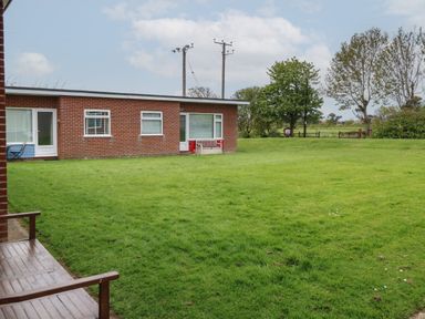 A grassy lawn with a wooden bench and brick buildings with doors and windows in the background at En-Casa in Mundesley