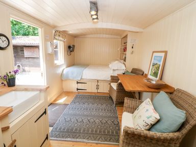 A small room with a bed a wooden table and wicker chairs a sink and a rug on the floor at Shepherd's Hut in Castleton Peak District