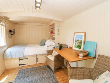 A small room with a bed under a window a wooden table with two wicker chairs and framed artwork at Shepherd's Hut in Castleton Peak District