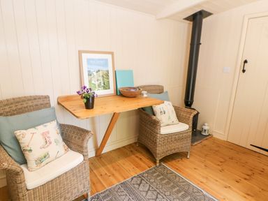 A small sitting area with two wicker chairs and a wooden table against a paneled wall at Shepherd's Hut in Castleton Peak District