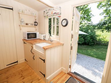 A small kitchen area with a microwave toaster kettle sink and shelves near an open door showing a garden at Shepherd's Hut in Castleton Peak District