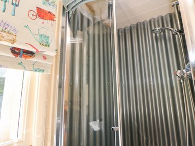 A shower with corrugated metal walls and a window with a curtain featuring garden tools at Shepherd's Hut in Castleton Peak District