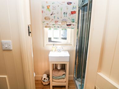A small bathroom with a sink on a stand and folded towels below a window with patterned blinds at Shepherd's Hut in Castleton Peak District