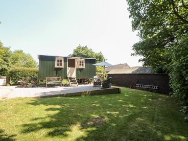 A small green shepherds hut with open windows in a garden with chairs and an umbrella at Shepherd's Hut in Castleton Peak District