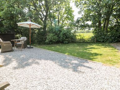 A garden area with gravel patio seating umbrella trees and a wooden gate at Shepherd's Hut in Castleton Peak District