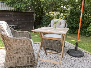 An outdoor seating area with two wicker chairs and a small wooden table with flowers on a gravel surface at Shepherd's Hut in Castleton Peak District