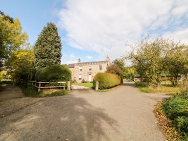 A stone house with a driveway and trimmed bushes surrounded by trees at Shepherd's Hut in Castleton Peak District