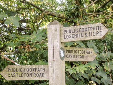 A wooden signpost with directions for public footpaths surrounded by green foliage at Shepherd's Hut in Castleton Peak District