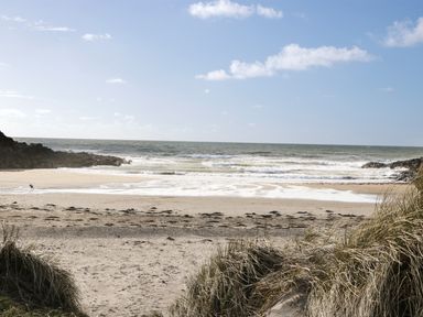 A sandy beach with seaweed and rocks on the shore with waves and a partly cloudy sky at Plas Bach in Aberffraw