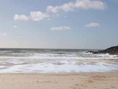 A sandy beach with waves and rocks on the side under a blue sky at Plas Bach in Aberffraw