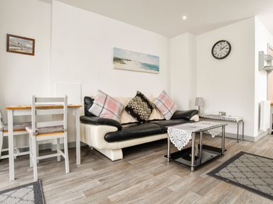 A living room with a black and white sofa and pillows a coffee table a dining table with chairs a wall clock and a painting at Plas Bach in Aberffraw