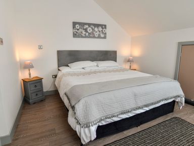 A bedroom with a double bed two bedside tables with lamps and a painting above the bed at Plas Bach in Aberffraw