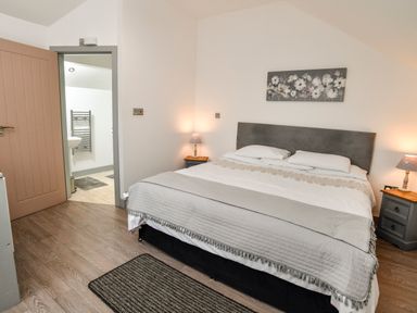 A bedroom with a large bed bedside tables and lamps a door leading to a bathroom at Plas Bach in Aberffraw