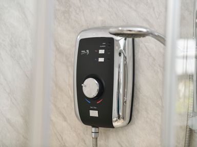 A close-up of a wall-mounted electric shower unit with a showerhead in a bathroom at Plas Bach in Aberffraw